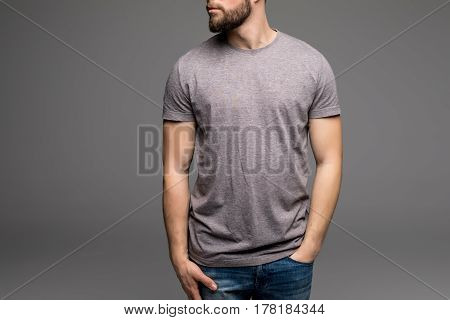 A Man In A Grey T-shirt And Denims Holds His Hands In Pockets.