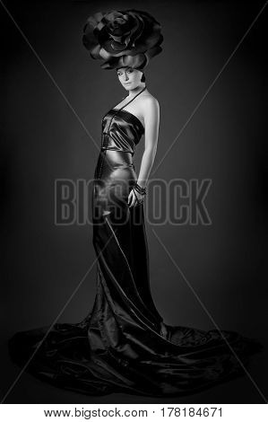 black and white Full-length dark portrait of a girl in a black dress and a rose hat.