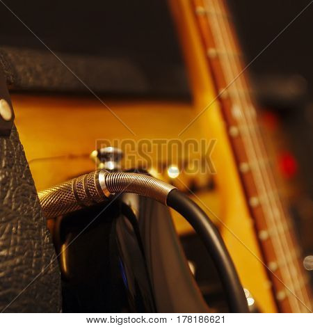 Input jack inserted to amplifier for electric guitar with guitar on the black background. Shallow depth of field low key close up. Focus on input jack.