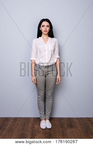 Front View,  Full Portrait Of Young Charming Calm Lady With Rolled Up Sleeves Standing Against Gray