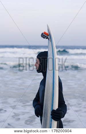 Wet athletic surfer with surfboard after riding. He wears a wetsuit or waterproof suit