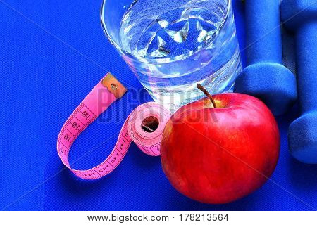 Close up of a pristine red apple two dumbbells  and glass water, blue atheletic small rug of   with reflection , sound lifestyle