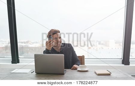 Attractive and handsome businessman call with mobile phone caucasian top manager having a phone talk wealthy man talking on the smart phone seated in the glass window walls office at his work break