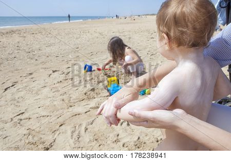 Mother applying sun cream to her baby while her daughter play on sand Huelva Spain