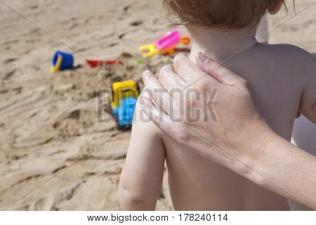 Mother applying sun cream to her baby on back with beach toys at bottom Huelva Spain