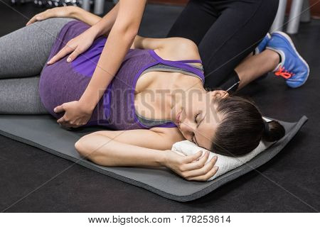 Trainer massaging pregnant woman on exercise mat