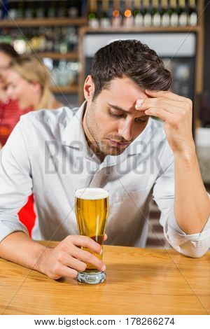 Tired man holding a beer while head in hand and sitting in a bar