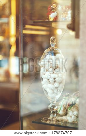 Rich variety of white chocolates candies in glass jars in display window of typical italian pastry shop in the street of Florence with light reflection on window