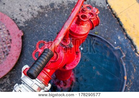 Red fire hydrant in the open manhole with connected hose. Top view. Close-up.