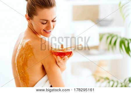 Happy Young Woman Sitting On Massage Table With Honey Plate