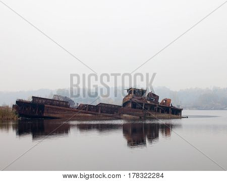 Old rusty sunken ship in water in a foggy day.