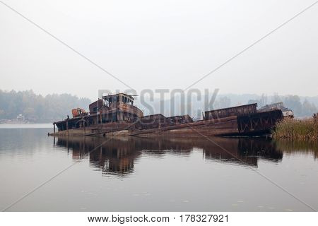 Old rusty sunken ship in water in a foggy day.