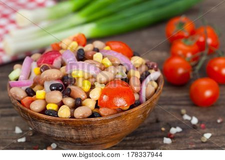 Salad made of beans, chickpeas and corn with spring onions and cherry tomatoes. Wooden background.