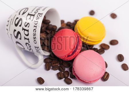 Colorful delicious French macaroons on coffee beans , Cup with coffee beans on white background
