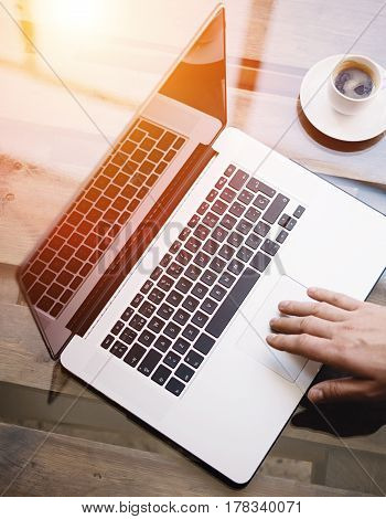 Man working with laptop at sunny office.Male hand pointing on notebook trackpad.Modern notebook, cup of black coffee on the wooden table.Reflections on glass surface.Vertical.Top view.Visual effect