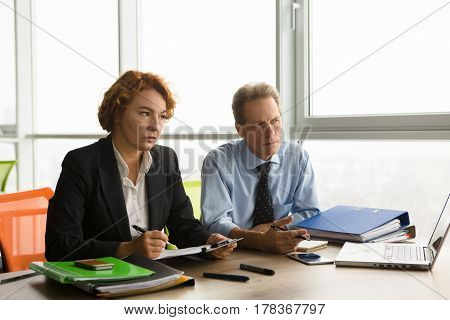 Two business representatives of huge company, firm or enterprise taking interview while sitting at table in board room all together. Serious business workers listening to new worker.