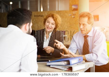 Toned of happy HR specialists smiling while taking interviews in office. Business representatives asking young man several questions connected with their company.