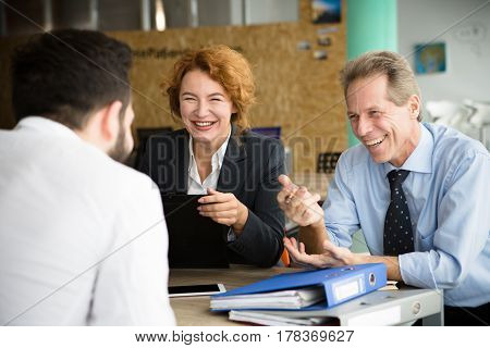 Happy smiling HR specialists communicating with young man in office. People asking about previous experience and jobs. Business concept.