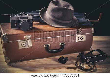 Adventure concept. Old film camera with vintage hat and umbrella on old suitcase neat film and camera case. Vintage toned.