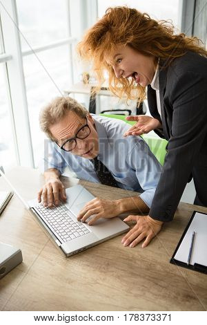 Mobbing, stress, work, scandal concepts. Angry red haired boss woman screaming at her worker in office. Businessman having stress while lying on laptop computer.