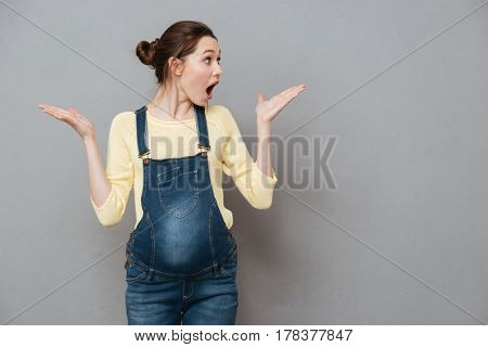 Image of happy surprised pregnant woman posing isolated over grey wall. Looking aside and holding copyspace on hands.