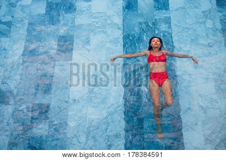 Top view aerial photo of a seductive sexy model in white swimwear is enjoying relax in hotel pool during her summer weekend. Amazing fashion woman in bikini having luxury spa rest.