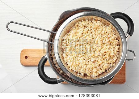 Colander with brown rice in saucepan on wooden board