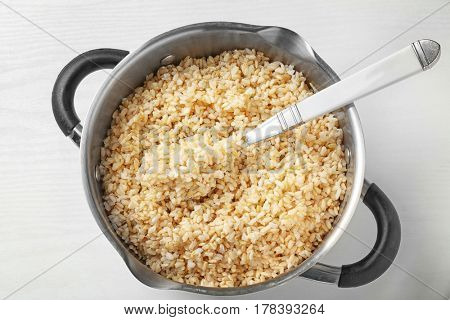 Pan with boiled brown rice on white background