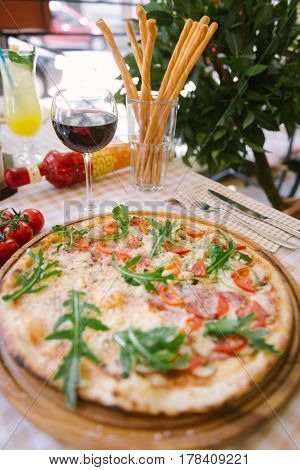 Pizza with cheese, tomato and meat, with glass of wine on served table with plaid tablecloth