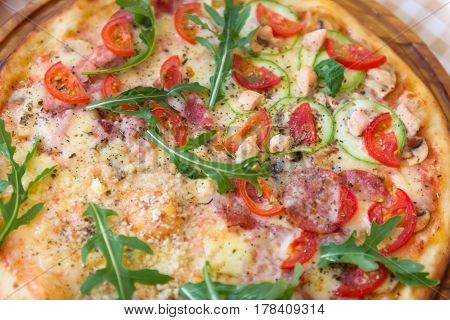 Pizza with cheese, tomato, squash, petals of arugula and meat, closeup