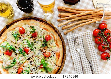 Tasty pizza with cheese, tomato and meat, with glass of beer and thin baguette on served table with plaid tablecloth
