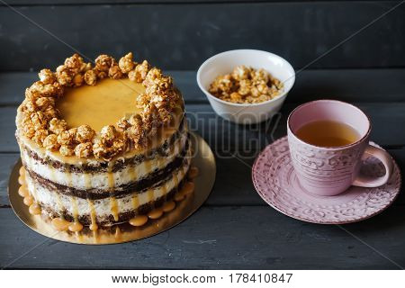 Delicious cake with caramel popcorn and caramel sauce and plate with popcorn and pink cup of tee