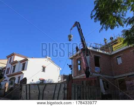 Alora Spain - March 24 2017: Men waiting for container of concrete being lifted onto building site roof