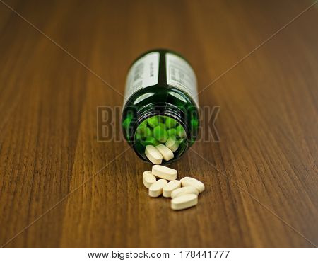 View of glass with pills lying on a wooden background