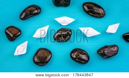 White paper boats in sigle file between abstract rock stones on blue background. Shot from Top Perspective.