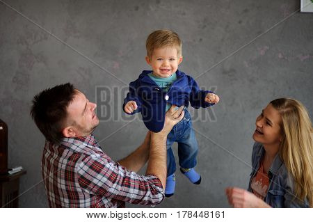 Young parents play with the little son. The kid joyfully laughs. The father and mother look at the child with love and tenderness.