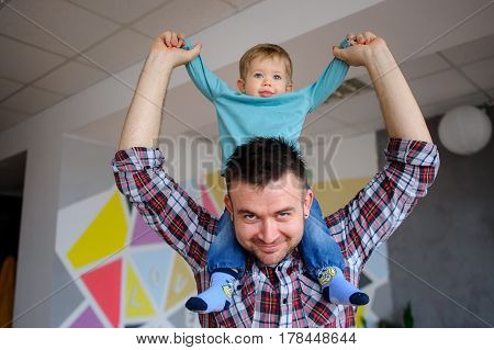 Little boy sits on the shoulders of his father. Young man playing with a child. Both the daddy and the kid smile.