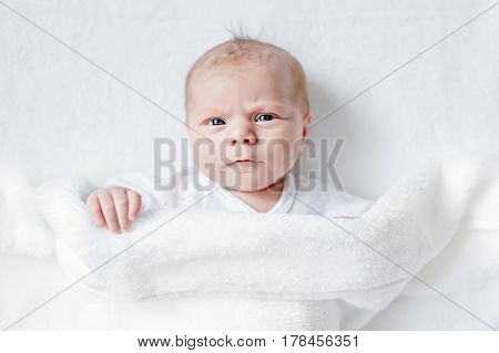 Cute adorable newborn baby in white bed and wrapped in blanket. New born child, little girl looking surprised at the camera. Family, new life, childhood, beginning concept.