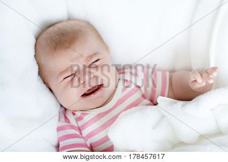 Cute adorable two months baby sucking fist and crying as getting first tooh. Closeup of crying child, little baby girl. Wrapped in white blanket. Family, birth, new life. Attentive child.