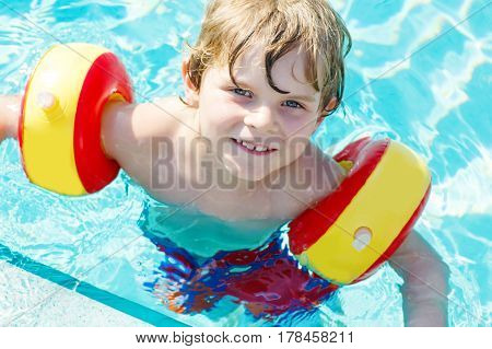 happy little kid boy having fun in an swimming pool. active happy child learning to swim. with safe floaties or swimmies. family, vacations, summer concept.