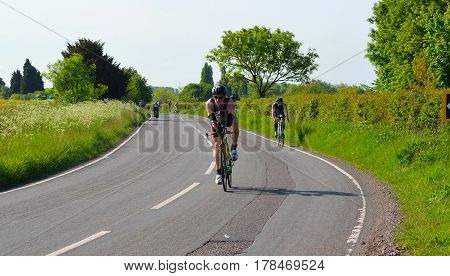GRAFHAM, CAMBRIDGESHIRE, ENGLAND - MAY 22, 2016:  Triathletes on road cycling stage of triathlon fields and trees in background.