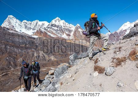 Group of Hikers with Backpacks and high Altitude climbing Gear walking up on steep Footpath snowy Summits View on Background