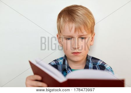 Education and school concept. A portrait of cute schoolboy with blond hair and attrractive blue eyes dressed in checked shirt holding a book preparing for the lessons isolated over white