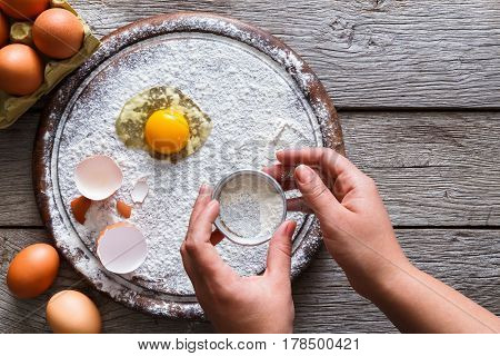 Baking concept. Yands sift sprinkled flour and eggs on wooden cutting board near knife, cooking ingredients. Prepare for making yeast dough. Top view, copy space