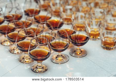 Row of glasses with whiskey or cognac on the table. Strong alcohol in a bar or restaurant. Transparent glasses with an alcoholic drink