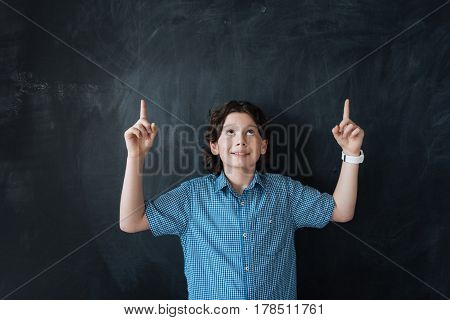 Just make the right choice. Helpful delighted glad boy standing against black background and enjoying imaginary drawing while pointing above