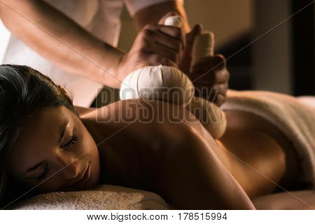 A young woman enjoys massage with herbal balls. Luxury spa treatment