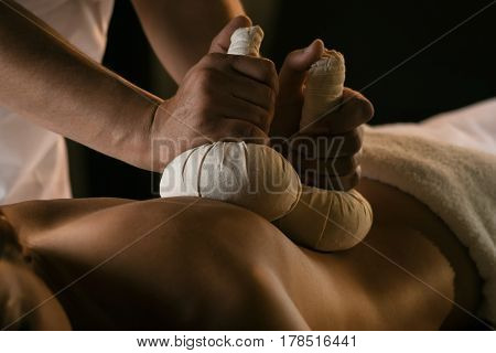 A young woman enjoys massage with herbal balls. Luxury spa treatment
