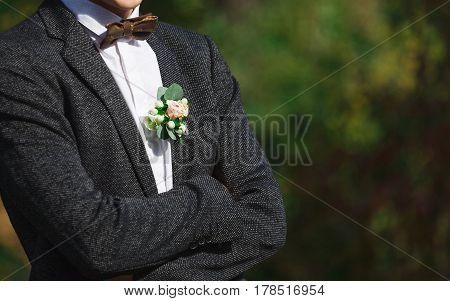 Wedding suit and accessories. Groom in outfit - shirt, bow-tie and jacket with floral buttonhole standing in the garden, close-up, crop, outdoors
