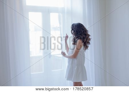 girl in white dress stands at the window curls hairstyle